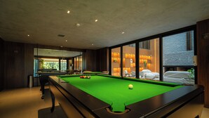 Una mesa de billar con bolas, un cubo de basura y una ventana con vistas al exterior.