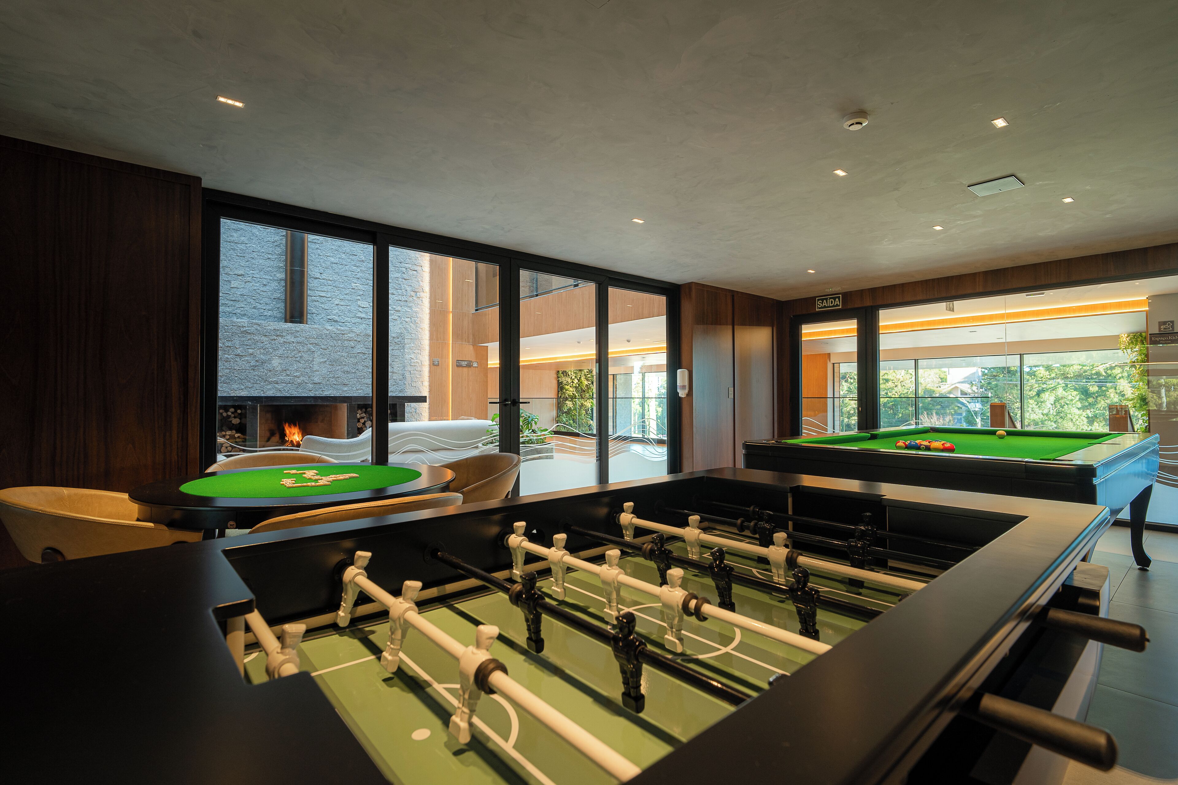 A room with a foosball table, a pool table, and a fireplace.
