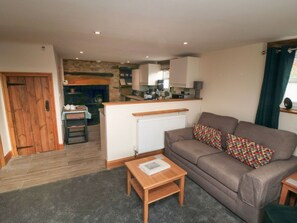 A living room with a sofa, a coffee table, and a kitchen in the background. - Crumbles Hideaway, Kirkbymoorside (York)