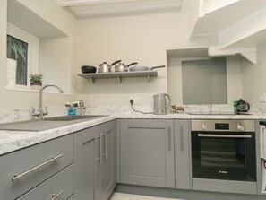 Een keuken met grijze kastjes, een Bosch oven, een spoelbak en een plank boven het aanrecht.