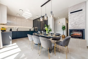 Una cocina moderna con comedor, que incluye una isla grande, luces colgantes y una chimenea.