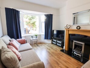 A living room with a sofa, TV, fireplace, and a window with curtains. - 13 The Crescent, Rhos-On-Sea (Bae Colwyn)