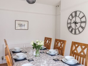 A dining room with a table set for four, a large wall clock, and a framed picture on the wall. - 13 The Crescent, Rhos-On-Sea (Bae Colwyn)