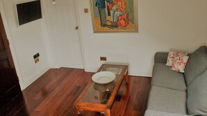 A living room with a wooden coffee table, a gray sofa, a painting on the wall, and a chandelier. - Peaceful 1-bedroom apartment in welcoming London neighborhood (London)