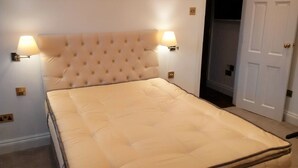 A bed with a tufted headboard, two wall-mounted lamps, and a door to the right. - Peaceful 1-bedroom apartment in welcoming London neighborhood (London)