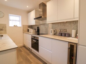 A modern kitchen with white cabinets, a stainless steel range hood, a microwave, a kettle, and a built-in oven. - Ted's Cottage, Skipton 2 bed (Skipton)