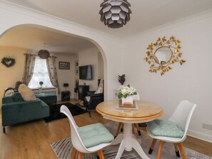 A living room with a green sofa, a round glass table with two chairs, a decorative mirror, and a wooden ceiling light. - Ted's Cottage, Skipton 2 bed (Skipton)
