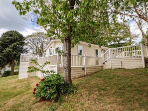 Ein Bungalow mit Veranda, einer kleinen Terrasse und einem weißen Zaun.