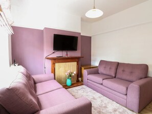 Sala de estar com dois sofás, uma televisão de tela plana na parede, lareira e um vaso com flores.