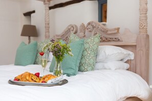 A bed with a tray of pastries, a glass of champagne, and a vase of flowers. - Wesley Barn, Cubert, Cornwall. (Newquay)