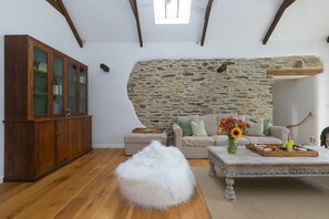 Une pièce avec un mur en pierre, un meuble en bois, un pouf blanc et une table basse décorée de fleurs.