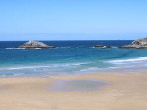 Une plage avec une eau d’un bleu limpide, un rivage sablonneux et des affleurements rocheux.