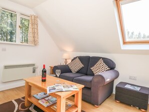 A cozy living room with a sofa, a coffee table, a lamp, and a window with curtains. - The Roost, East Tytherley (Salisbury)