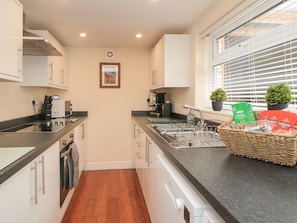 A modern kitchen with white cabinets, a black countertop, a built-in oven, and a window with blinds. - Westgate, Guisborough (Guisborough)