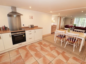 A modern kitchen with a stainless steel range hood, a built-in oven, and a wooden countertop. There is a dining area with a white table and chairs, and a red sofa in the background. - The Nook at Timbers, Great Longstone (Bakewell)