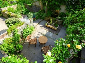 A garden patio with wicker furniture, a stone wall, and lush greenery. - The Nook at Timbers, Great Longstone (Bakewell)
