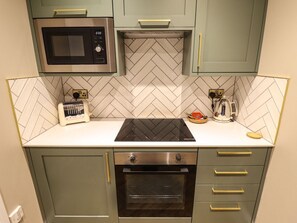 Een compacte keuken met een magnetron, broodrooster en oven, met een backsplash van visgraat tegels en lichtkleurige kastjes.