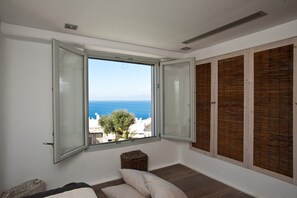 A room with a large window, a bed, a wicker basket, and wooden shutters. - Mykonos Cloud White Villa (Mykonos)