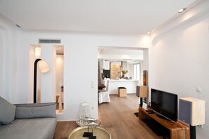 A modern living room with a sofa, TV, and a dining area in the background. - Mykonos Cloud White Villa (Mykonos)