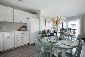 A modern kitchen with white cabinets, a white refrigerator, and a dining area with a round table and chairs. - Sunset Landing, peaceful water views and front-row seats to some of Ocean City’s stunning sunset (Ocean City)