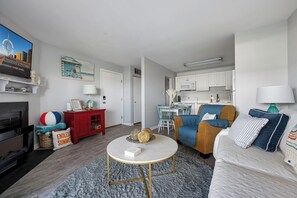 A modern living room with a sofa, coffee table, and a TV. There's a kitchen area with white cabinets and a dining table. - Sunset Landing, peaceful water views and front-row seats to some of Ocean City’s stunning sunset (Ocean City)