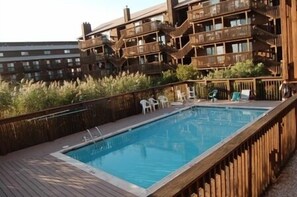 A pool with wooden deck and lounge chairs, surrounded by a wooden fence and a building with balconies. - Sunset Landing, peaceful water views and front-row seats to some of Ocean City’s stunning sunset (Ocean City)