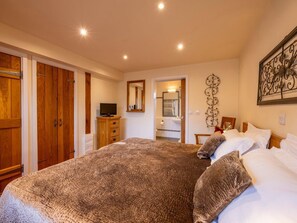 Un dormitorio con una cama grande, armario de madera, televisión y baño visible a través de una puerta abierta.