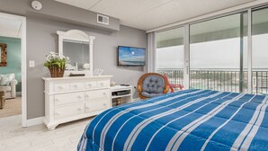 Un dormitorio con una cama grande, un aparador, una televisión y vistas a la ciudad desde un balcón.