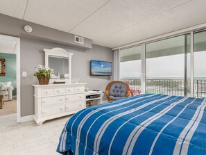 Ein Schlafzimmer mit einem großen Bett, einem Schminktisch, einem Fernseher und Blick auf die Stadt vom Balkon aus.