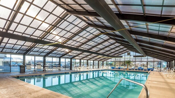 Una piscina interior con techo de cristal, agua transparente y zona de piscina con sillones de descanso.