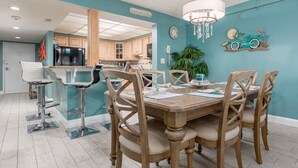 Un comedor con mesa y sillas de madera, una araña y una pared color aguamarina decorada con motivos de motocicleta.