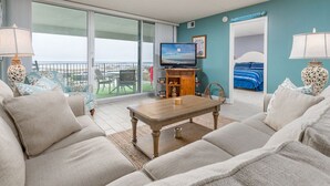 Habitación de hotel con balcón, televisor, cama y zona de estar con una mesita de centro.