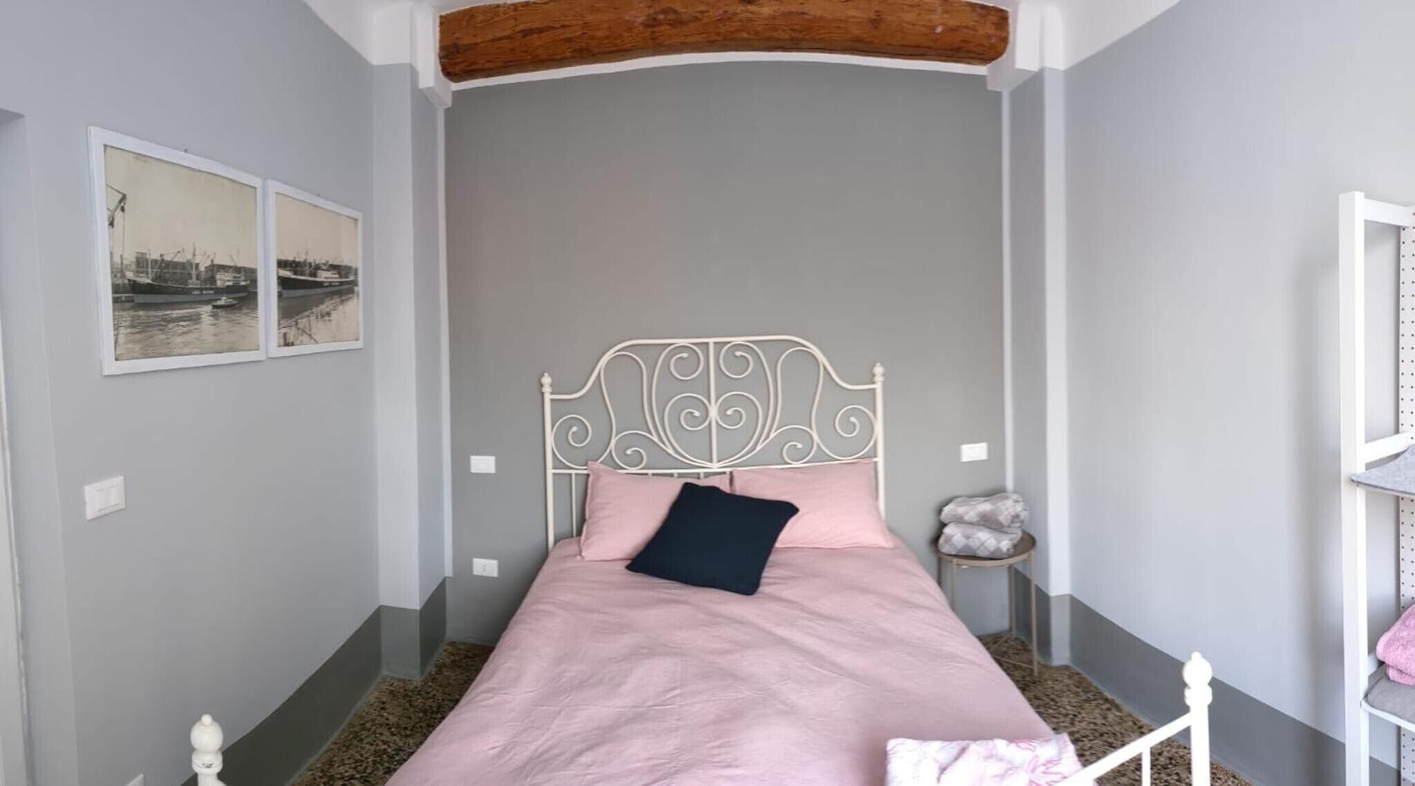 A bedroom with a bed, a headboard, a wall-mounted picture, and a wooden beam ceiling.