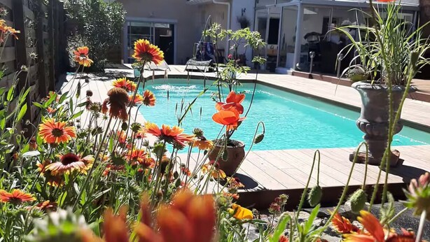 A backyard with a swimming pool, surrounded by various flowers and a house in the background. - 200 meters from the streetcar stop, room with shared bathroom, quiet! (Eysines)