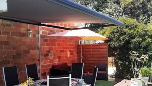 An outdoor patio with a brick wall, a table with chairs, and a covered area. - 200 meters from the streetcar stop, room with shared bathroom, quiet! (Eysines)
