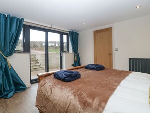 Un dormitorio con una cama grande, un ventanal corredero al exterior y una puerta de madera.