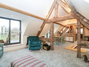 Una habitación estilo loft con vigas de madera a la vista, un sillón azul aguamarina, un tapete multicolor con diseño en zigzag y una zona de comedor con mesa y sillas.