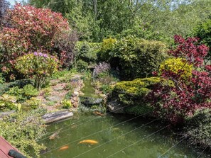 Un jardín con un estanque, diversas plantas y un puente de madera.