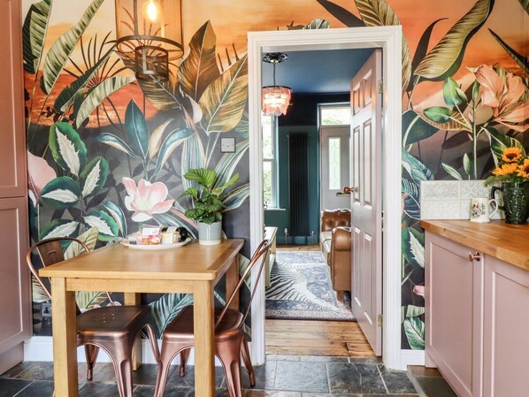 A kitchen with a dining table, chairs, a potted plant, and a mural with tropical leaves and flowers.