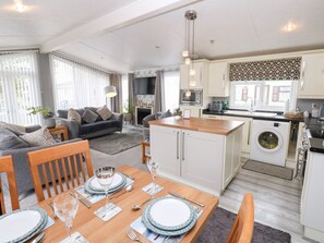 Une cuisine moderne avec des meubles blancs, un îlot central et un coin repas avec une table dressée pour quatre personnes.