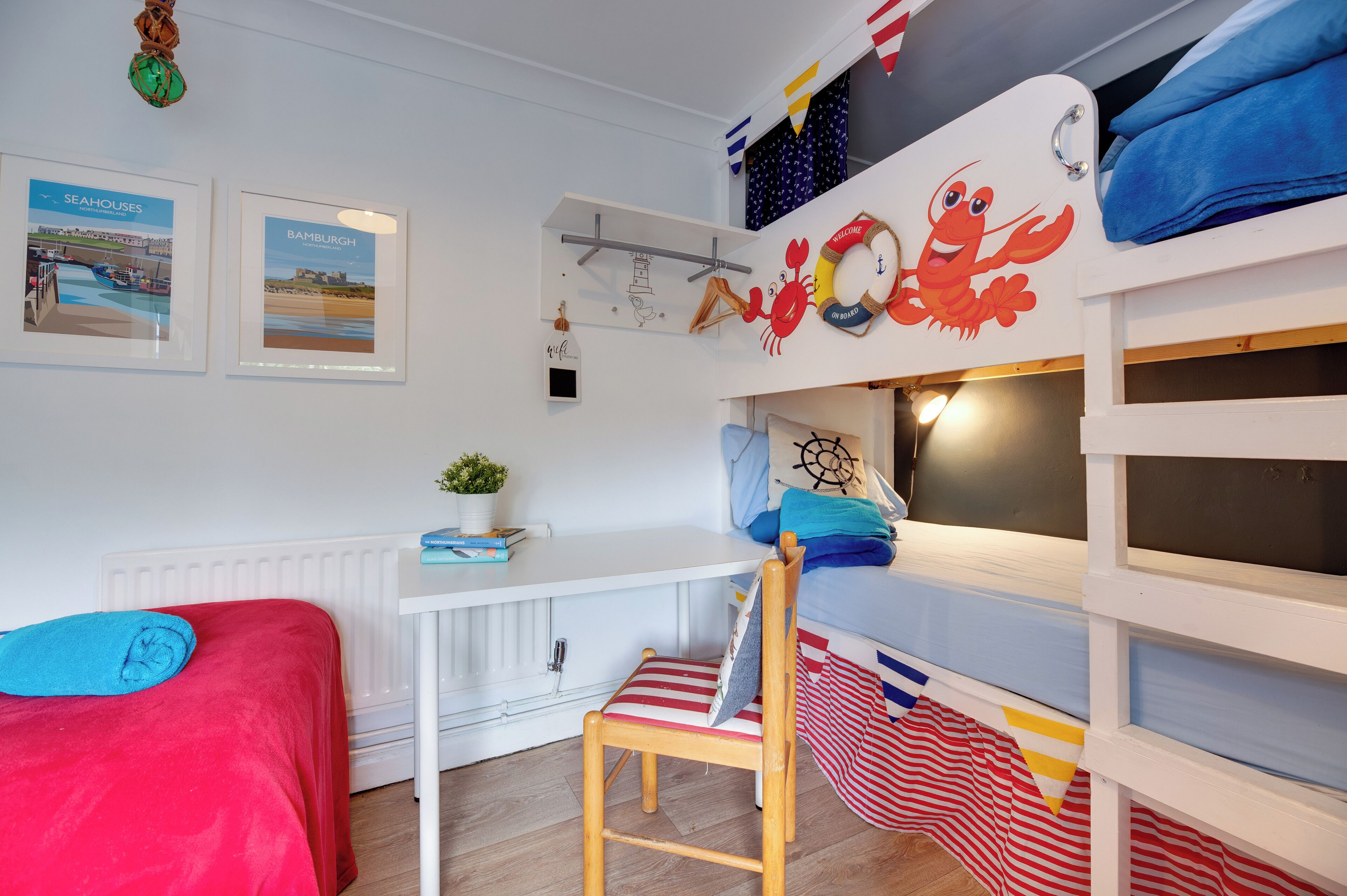A bunk bed with a crab decoration, a desk with a plant, and two framed pictures on the wall.