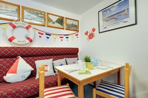 A cozy room with a patterned sofa, a small table with a plant, a framed picture, and a life ring on the wall.