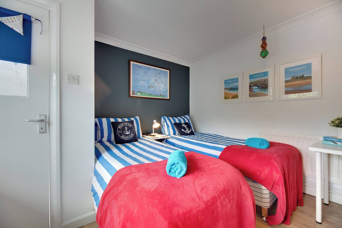 A room with two beds, a small table, a map on the wall, and framed pictures.