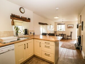 A kitchen with a Bosch dishwasher, wooden cabinets, a wooden countertop, a sink, and a dining area with a table and chairs. - Charming Lane Head Retreat in Cartmel (Grange-Over-Sands)