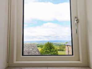 Una ventana con vistas a un paisaje rural, que incluye campos y un edificio lejano.