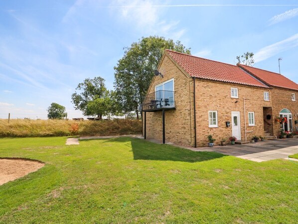 A brick house with a red-tiled roof, a balcony, and a well-maintained lawn.