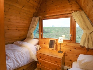 A wooden cabin room with two beds, a window with curtains, a dresser, and a lamp. - Rose Lodge, Milton On Stour (Gillingham)
