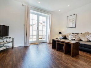 Ein Wohnzimmer mit Fernseher, Sofa, Couchtisch und einer Schiebeglastür, die auf einen Balkon führt.