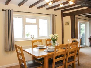 A dining area with a wooden table set for six, six chairs, and a vase of white flowers.