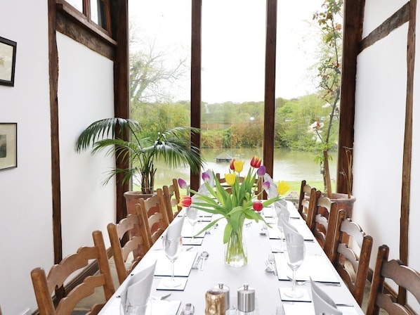 A dining table set for six with a vase of flowers, wooden chairs, and a view of a lake.